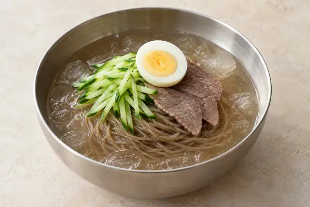 AI illustration: A deep steel bowl of thin brown cold noodles in clear chilled broth, cucumber matchsticks.