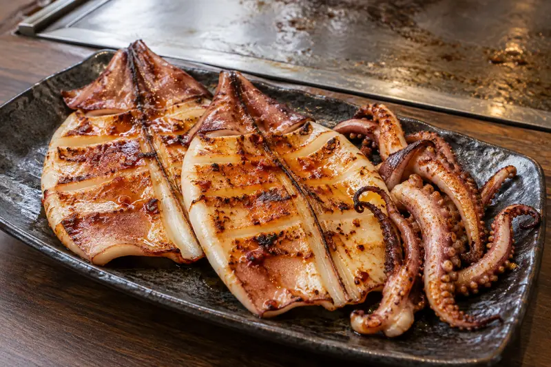 AI illustration: Griddle-cooked squid with lightly charred edges and brushed seasoning.