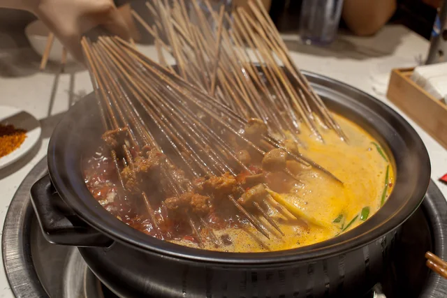 Bamboo skewers of meat cooking in a steaming chuanchuan hotpot with red and pale broth.