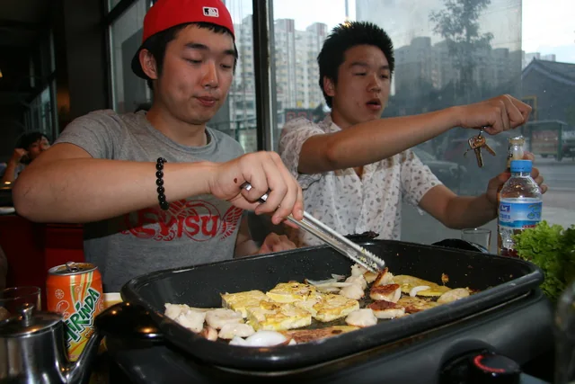 Diners cooking food on a tabletop grill at a Qiqihar barbecue meal.