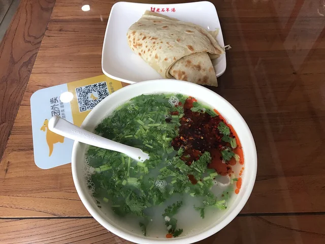 A bowl of lamb-offal soup with herbs and chili, served with bread.