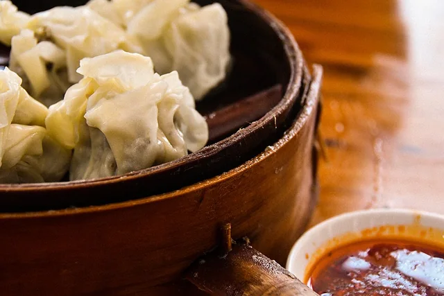 Leshan shaomai dumplings in a bamboo steamer, with dipping sauce alongside.