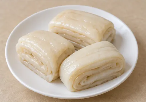 Sweet Layered Lard Rolls (脑髓卷): Glossy ivory rectangular steamed rolls with folded layers and translucent sweet-fat filling, no brain or meatball centre. AI dish illustration; not a restaurant photograph.