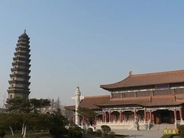 The courtyard of 宝相寺 at Wenshang: the tall brick 太子灵踪塔 with its many eaves at the left, a large hall with a red tiled roof and red columns at the right, a white carved stone pillar in the centre and trees along the front.
