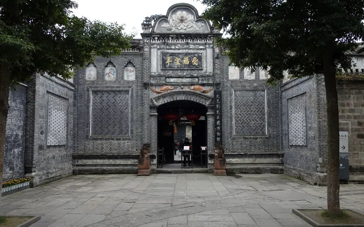 The gate front of 刘氏庄园: a grey brick wall with a carved arched doorway lettered 受福宜年 in gold, framed by relief panels and a scrolled crest, with stone drums at the steps, red lanterns inside the opening, and a paved courtyard.