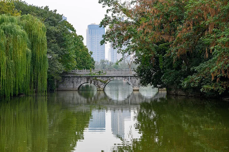 A bridge, water and willow-lined banks in Lord Bao Park, Hefei; 26 October 2019.