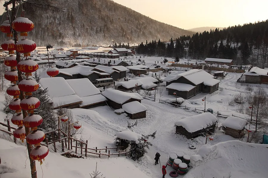 Snow-blanketed wooden cabins with rows of red lanterns at dusk