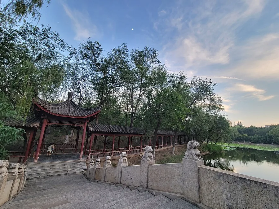 A long lakeside pavilion and stone bridge at Xigu Park, Tianjin. Photographed on 15 June 2024.