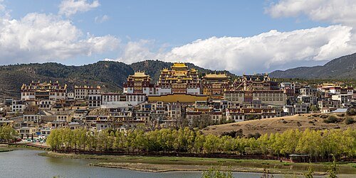 A large gold-roofed Tibetan Buddhist monastery complex on a hillside above a lake