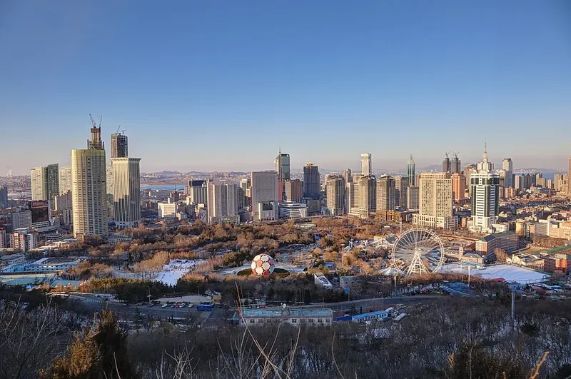 A city view in Xigang District, Dalian (大连西岗区), with parkland in the foreground.