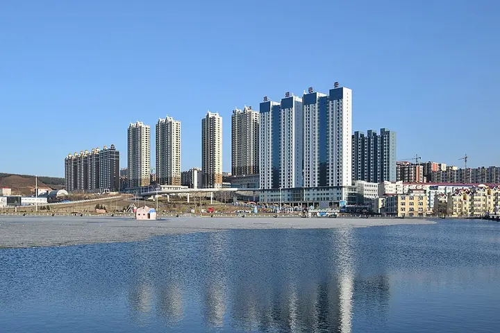 High-rise apartment towers of downtown Suifenhe reflected in a frozen park lake