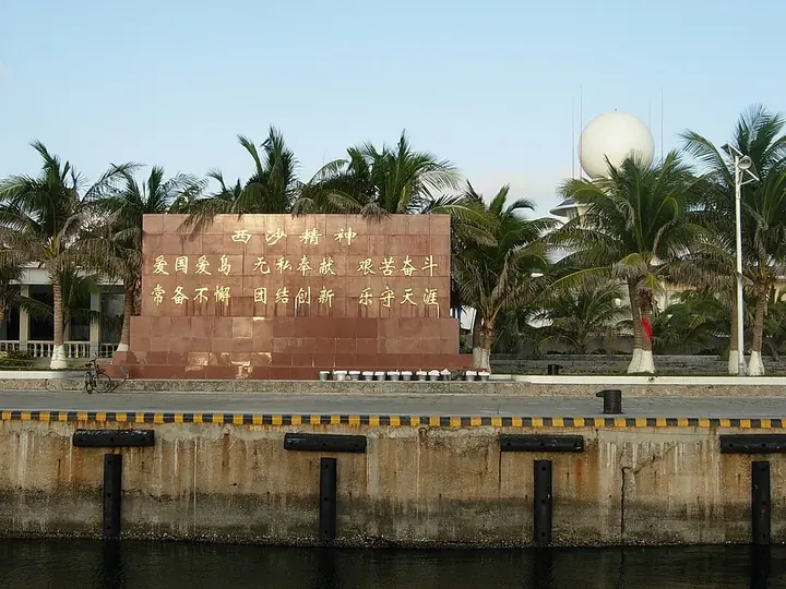 A stone monument inscribed with Chinese text among palm trees beside the waterfront
