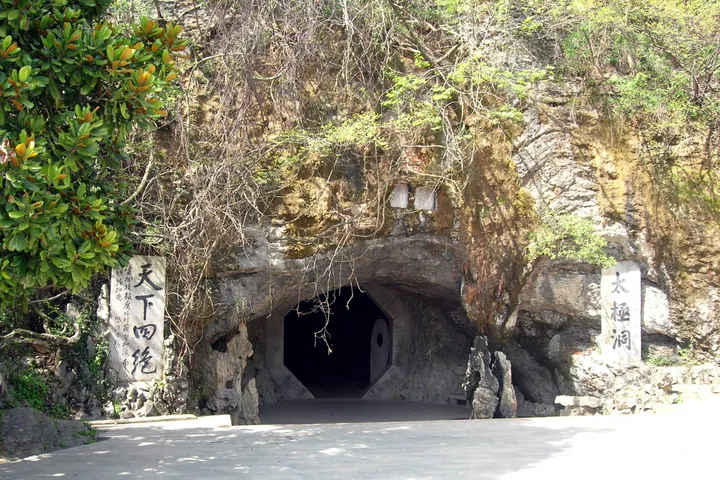 Octagonal stone cave entrance carved into a cliff, flanked by inscribed stone tablets.