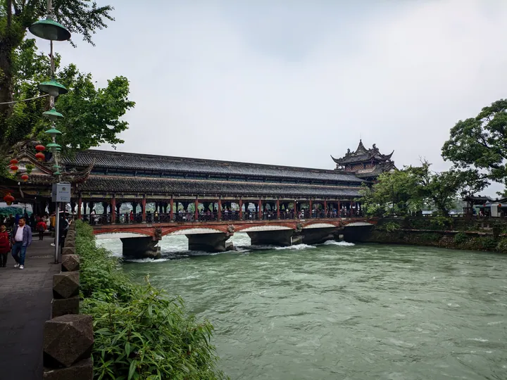 Covered wooden bridge with an ornate pavilion roof over rushing river water