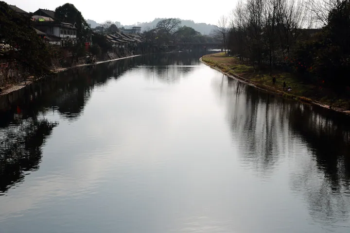 Calm canal reflecting old wooden riverside buildings in Pingle Ancient Town