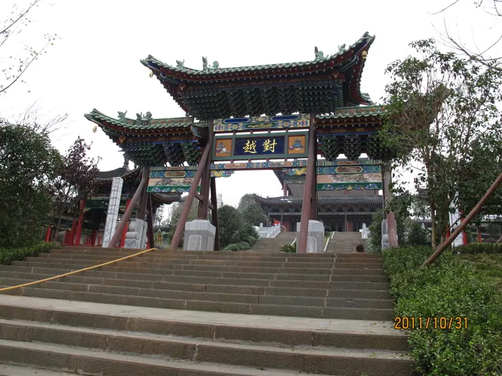 Colourful traditional Chinese archway gate at the top of a stone staircase, surrounded by trees.