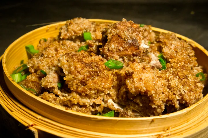 Bamboo steamer with slices of rice-flour-coated pork belly on greens