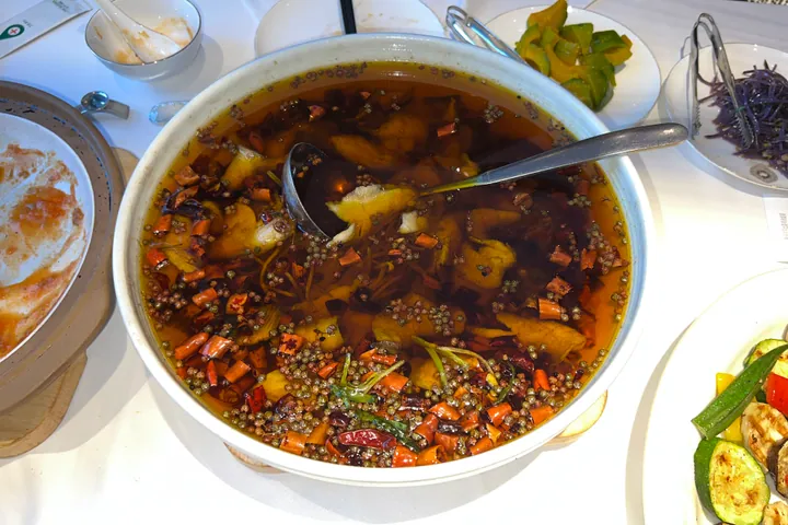 A large bowl of fish slices in red chili oil with floating dried chilies and peppercorns