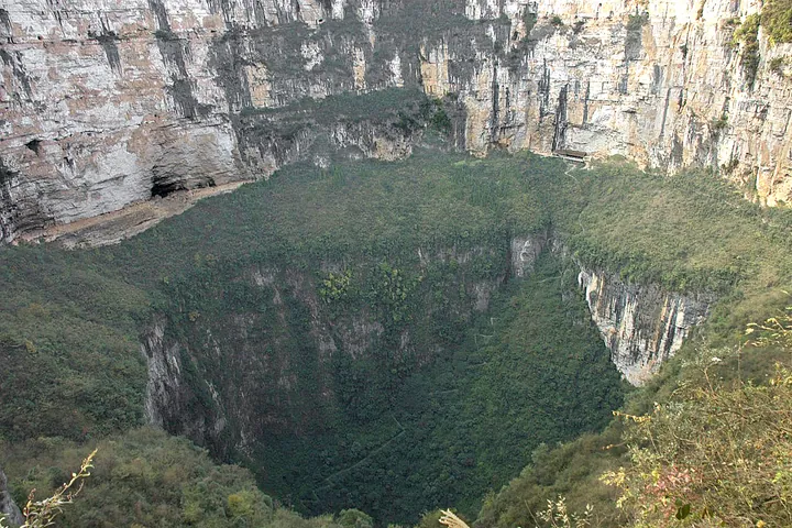 View down into the vast forested walls of the Xiaozhai Tiankeng sinkhole