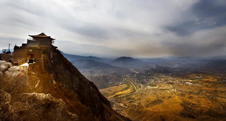 An ancient pavilion on a cliff top overlooking a valley and town below
