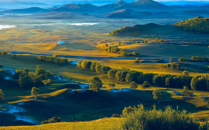 Rolling green grassland with a white yurt and hills lit by golden evening light