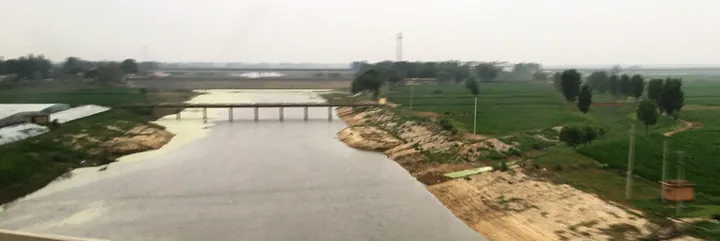A wide canal with a road bridge, farmland and trees