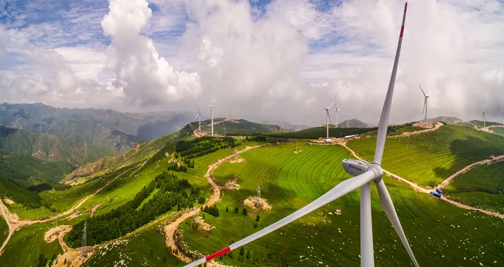 Wind farm on forested green hills under a partly cloudy sky in Guangling County