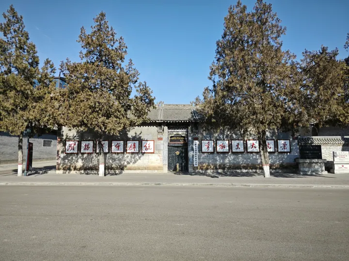 A traditional Chinese building facade with commemorative plaques, flanked by trees