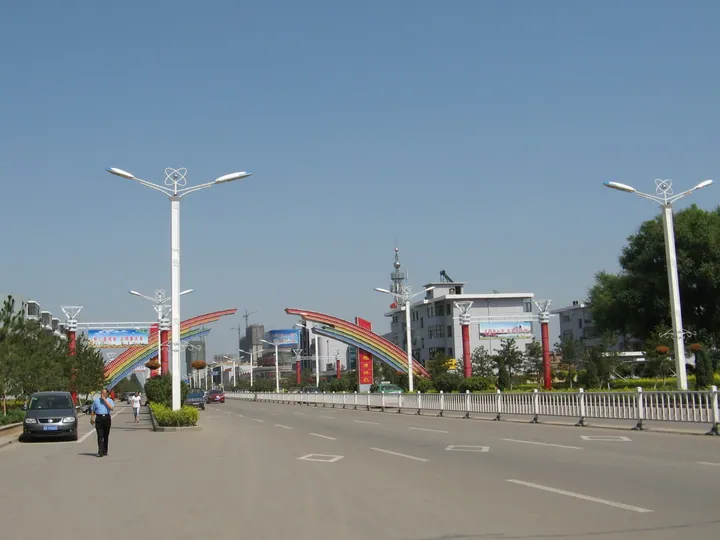 Wide city street with a decorative rainbow arch and buildings in Huairen
