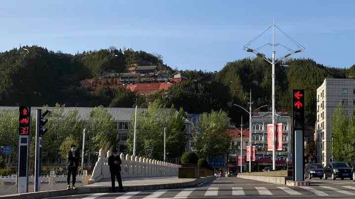 A city street with a temple-topped hill rising in the background in Lishi District