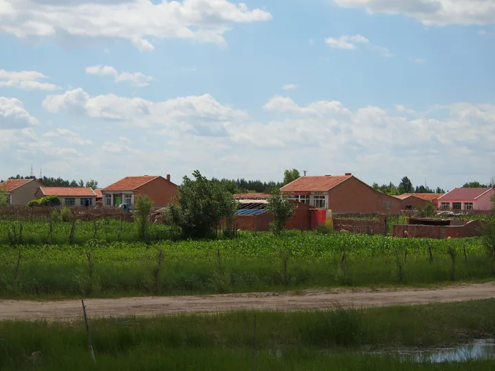 Brick farmhouses behind a field of crops in Horqin Left Back Banner