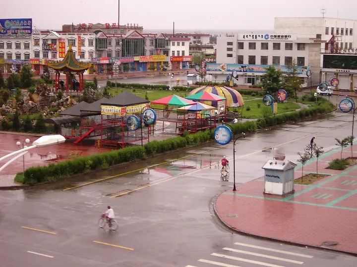A town square with a pavilion, colourful tents and shops on a rainy day