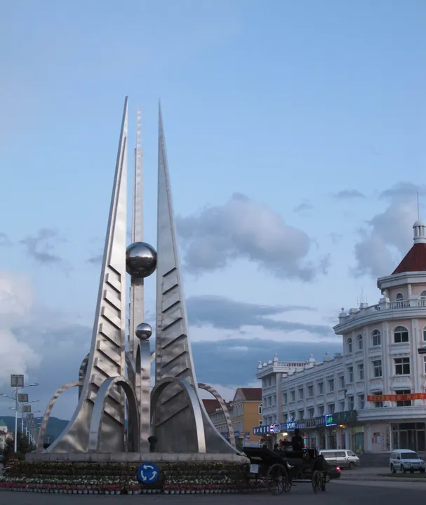 A modern sculpture and a colonial-style building in the town square of Arxan at dusk