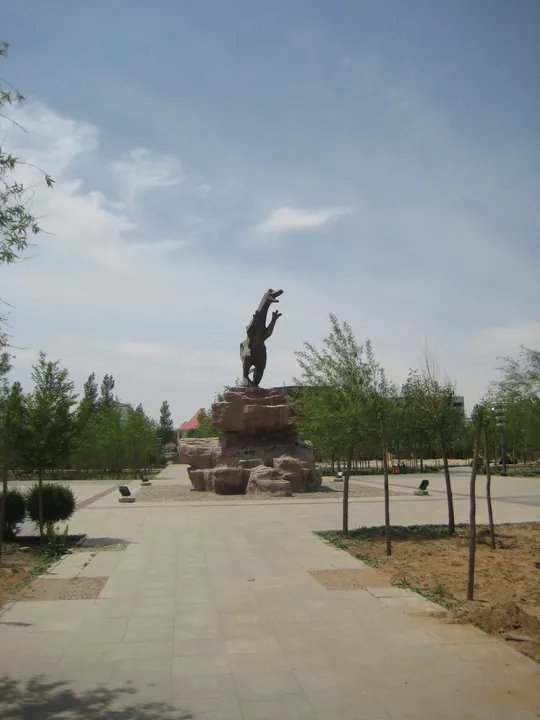 A bronze dinosaur statue on a rock outcrop in a landscaped park