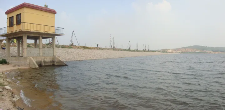 Yellow control building on a reservoir dam with water and distant hills