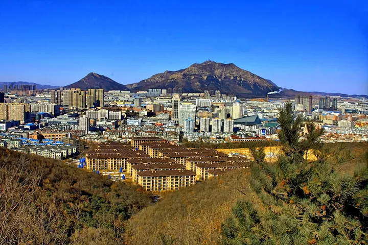 A city skyline in front of a large forested mountain under a clear blue sky