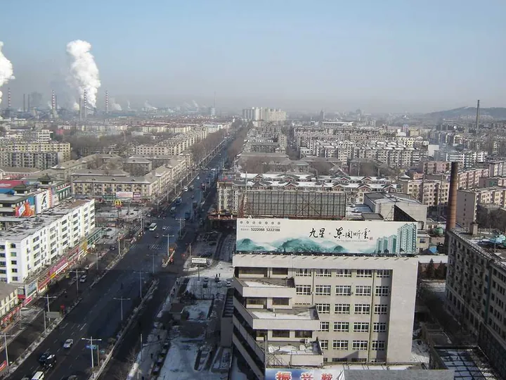 Aerial view of a main street lined with apartment blocks in Tiedong District, Anshan, with industrial smoke stacks in the distance