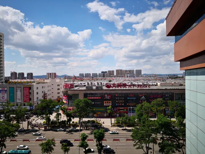 A rooftop view of a shopping mall and apartment towers under a partly cloudy sky in Fuxin