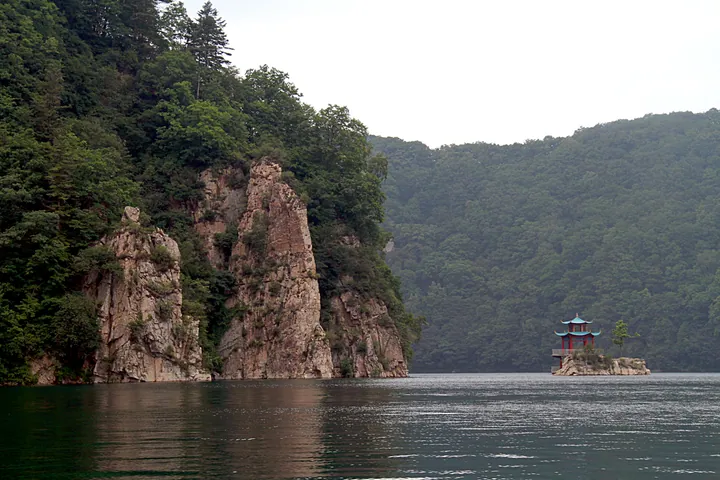 A crater lake surrounded by forested cliffs with a small pavilion on an island