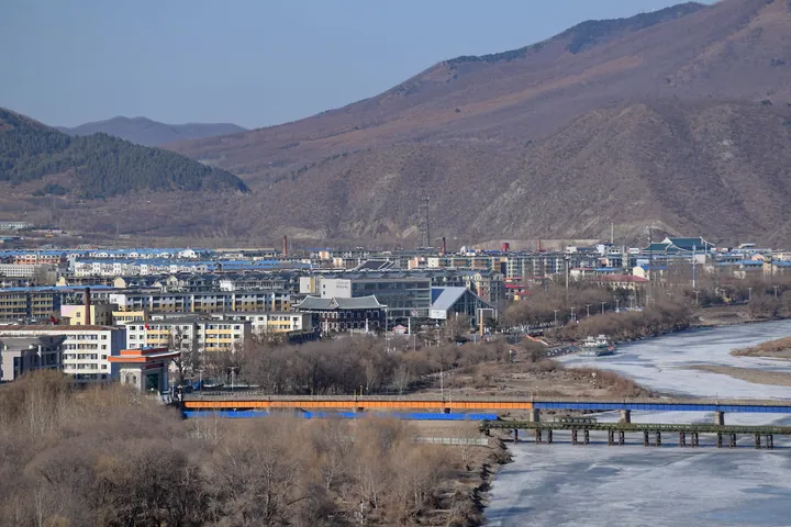 An aerial view of a riverside town with mountains and a bridge in Tumen