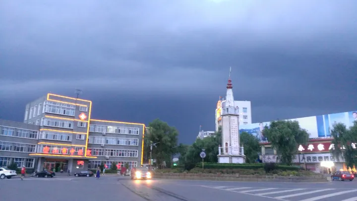 Illuminated buildings and a tower under a dramatic evening sky in Mishan
