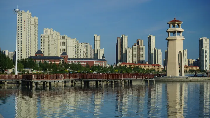 Lakeside promenade with a tower and apartment buildings reflected in the water