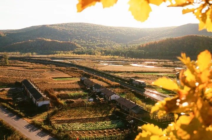 Golden autumn farmland, farmhouses and a train winding through a forested valley
