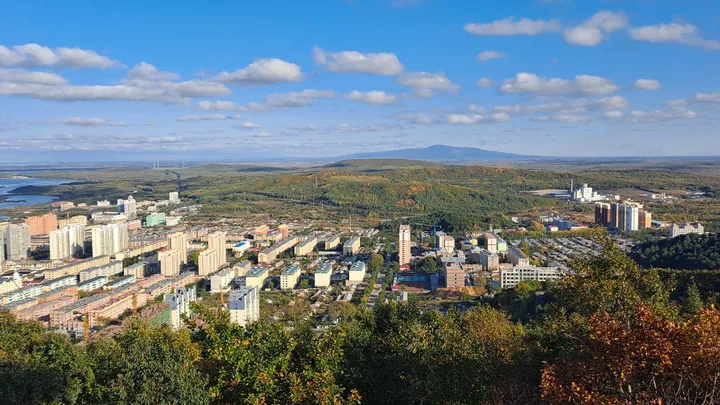 A city skyline seen from a hillside pavilion with green foliage in the foreground