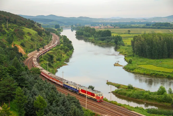 Elevated view of a river bend, forested hills and a train near Hailin