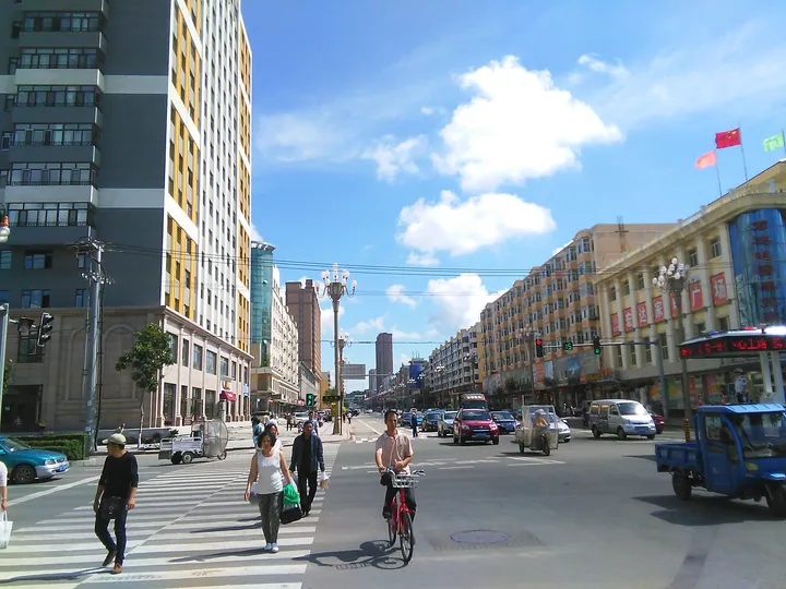 Busy city street with pedestrians, a cyclist and buildings under a blue sky in Bei'an
