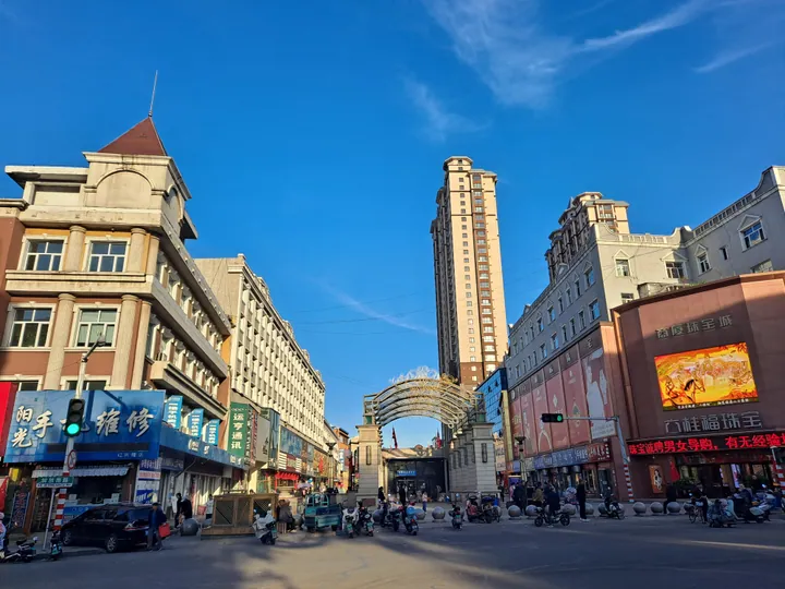 City street with an ornamental arch and a tall building under a blue sky in Qing'an County