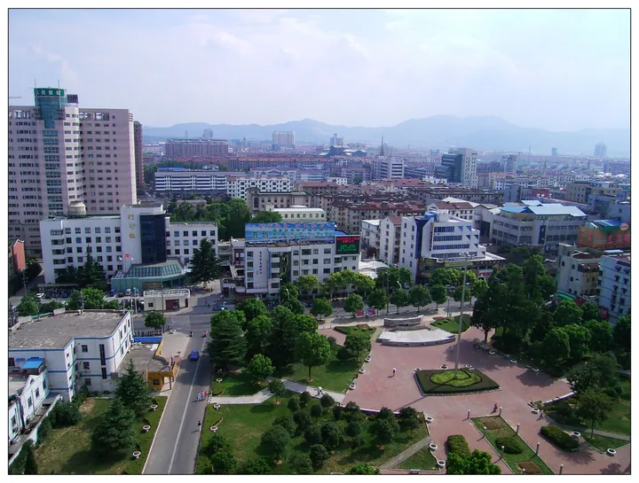 An elevated cityscape of Yixing with a plaza and distant hills