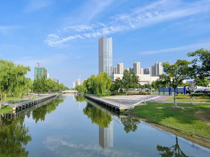 A canal reflecting a glass skyscraper and riverside towers in Tongzhou District, Nantong