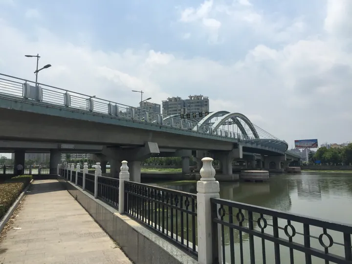 An arched steel bridge crossing a river with city buildings in the background in Funing County